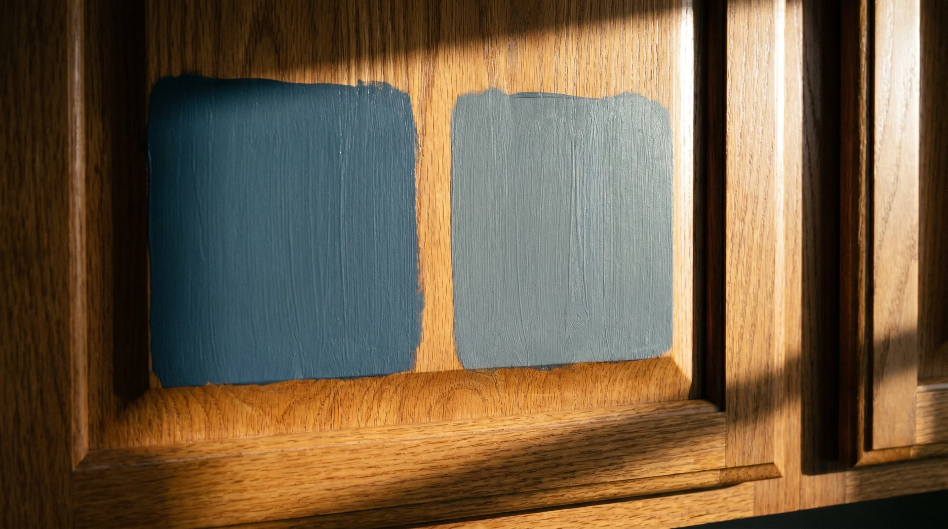 Blue and gray paint swatches on a cabinet door showing undertone shift in late-afternoon kitchen light
