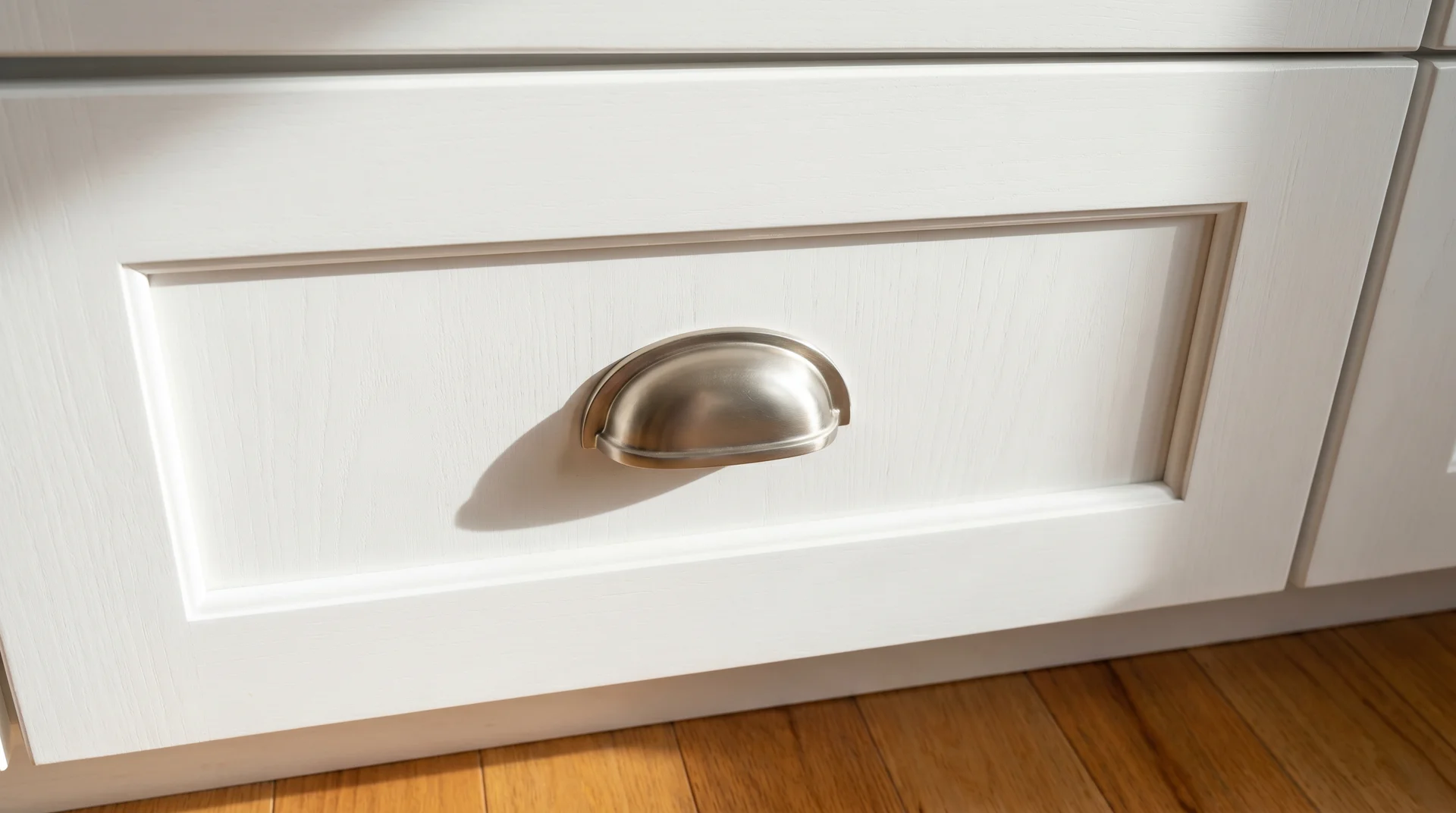 Brushed nickel cup pull on white shaker lower cabinet showing the U-shape grip depth and shadow against flat white paint 