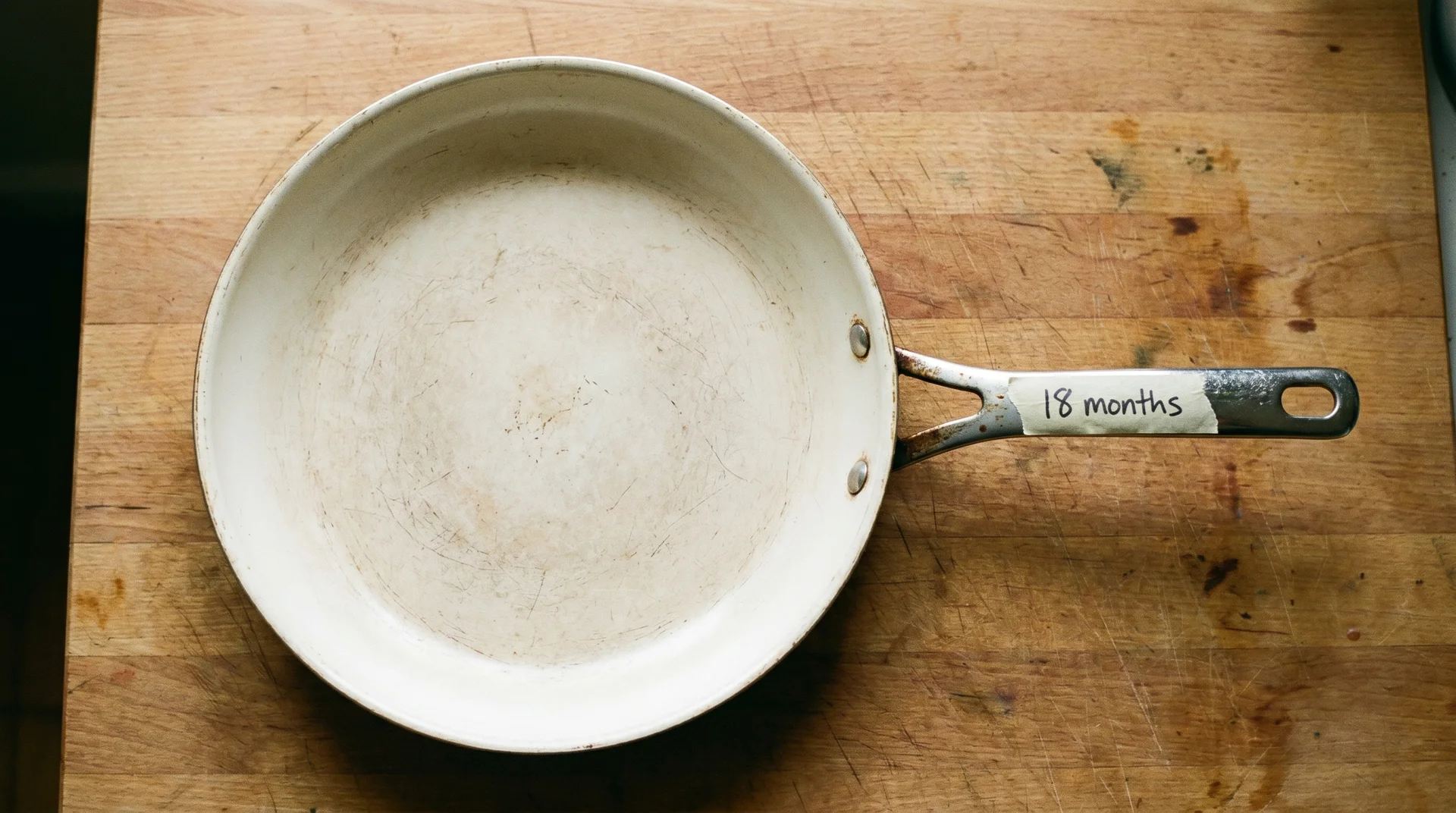 Ceramic nonstick pan with worn cooking surface on wooden countertop, natural light