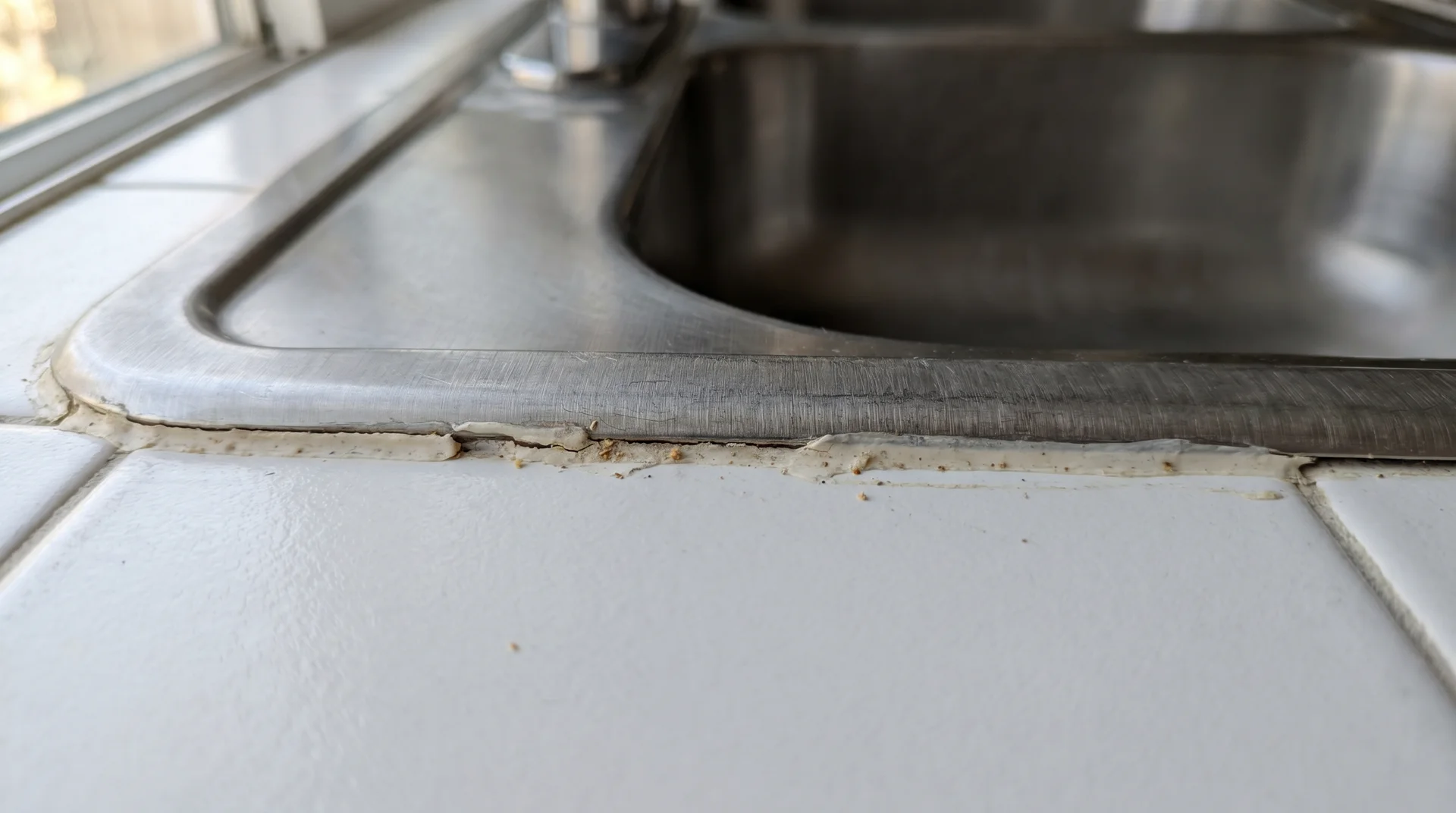 Close-up of discolored caulk seam between stainless steel sink rim and countertop where mold commonly establishes
