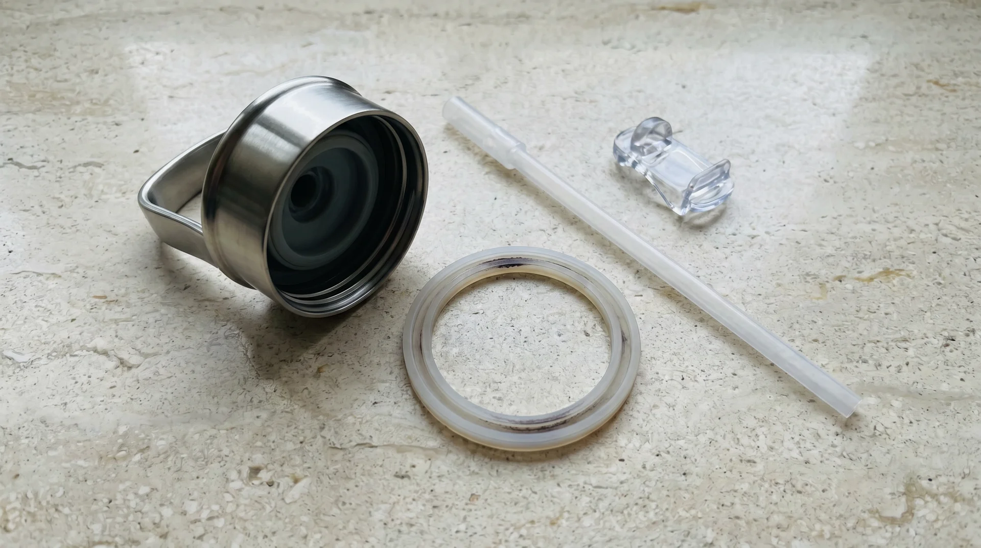 Disassembled stainless steel water bottle lid showing silicone gasket removed and laid flat beside lid components
