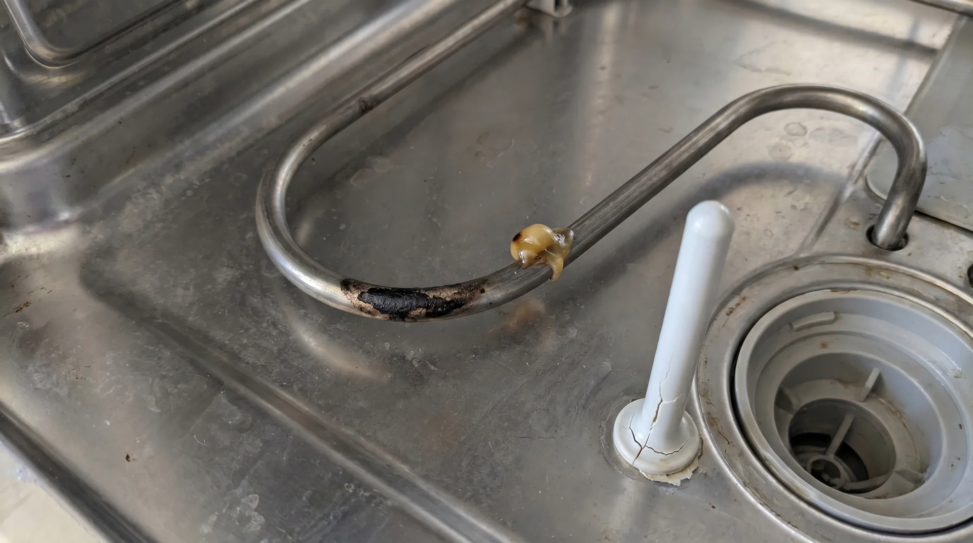 Dishwasher heating element coil with melted plastic residue and cracked rack tine coating visible
