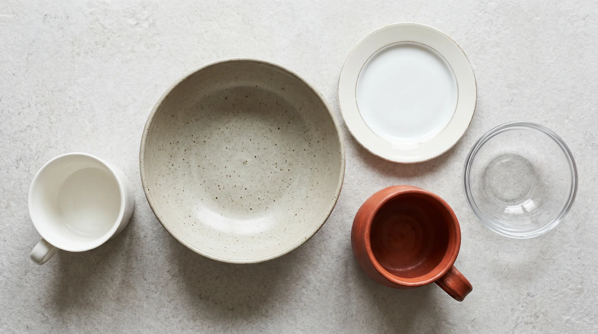 Five ceramic and glass dishes on grey stone showing material texture differences in microwave safety