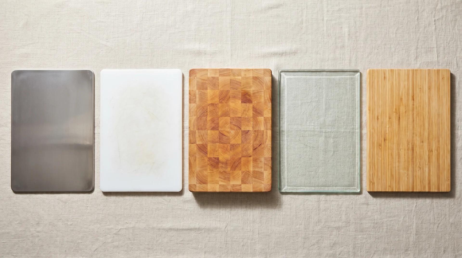 Five cutting board materials side by side: titanium, HDPE, maple, glass, and bamboo for comparison
