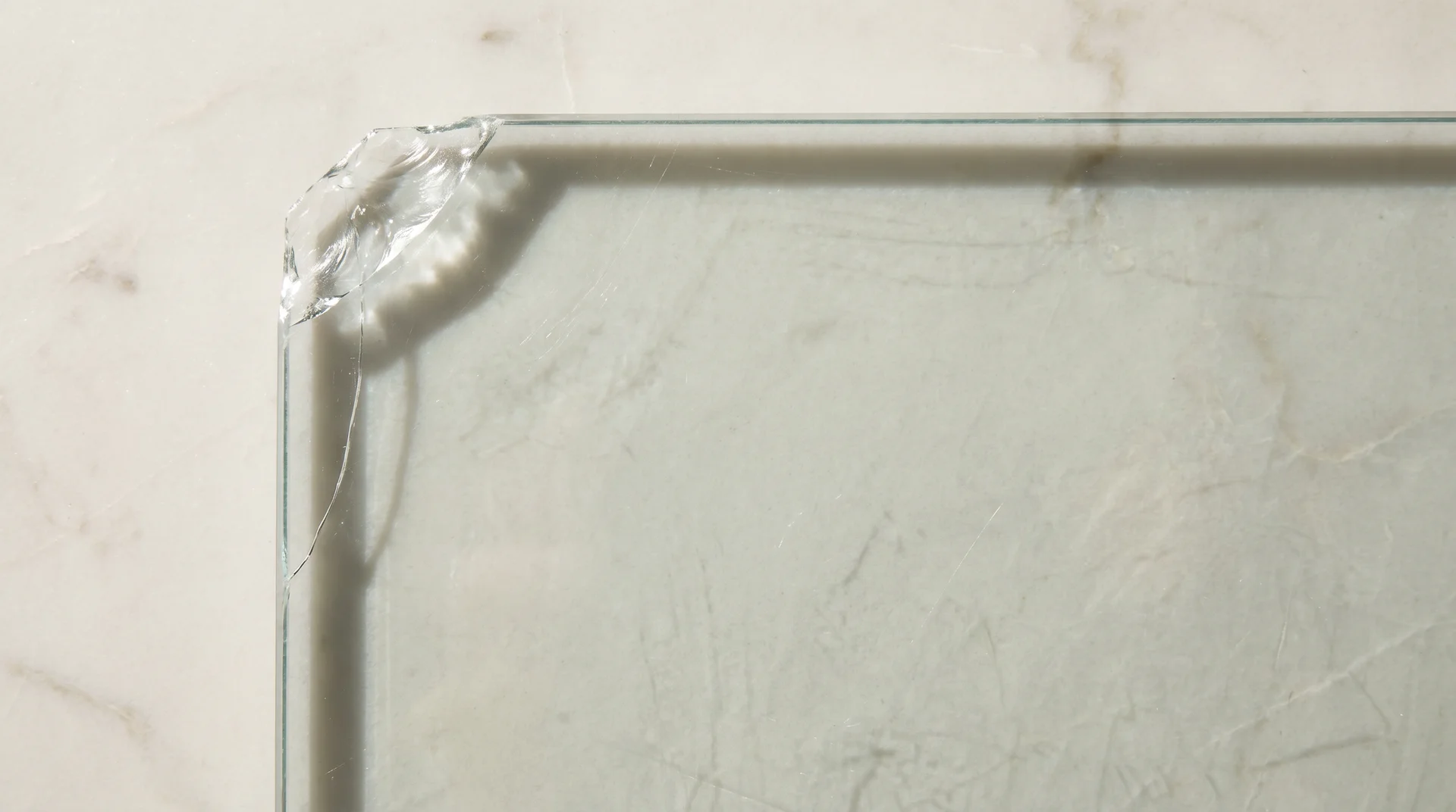 Glass cutting board showing a chip at the corner and hairline crack along the edge from normal kitchen use 