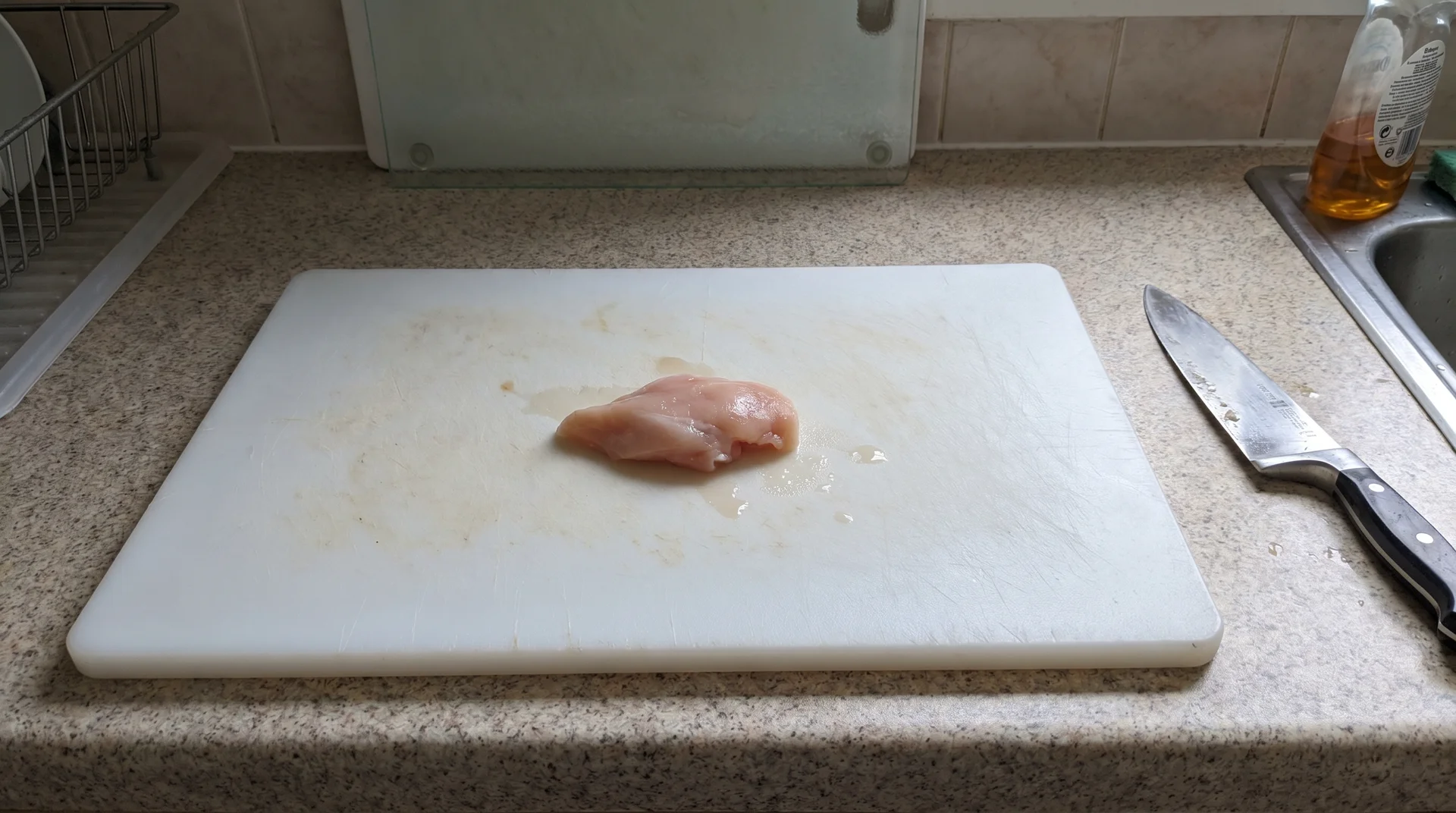 HDPE plastic cutting board used for raw chicken prep, with glass board stored unused in the background
