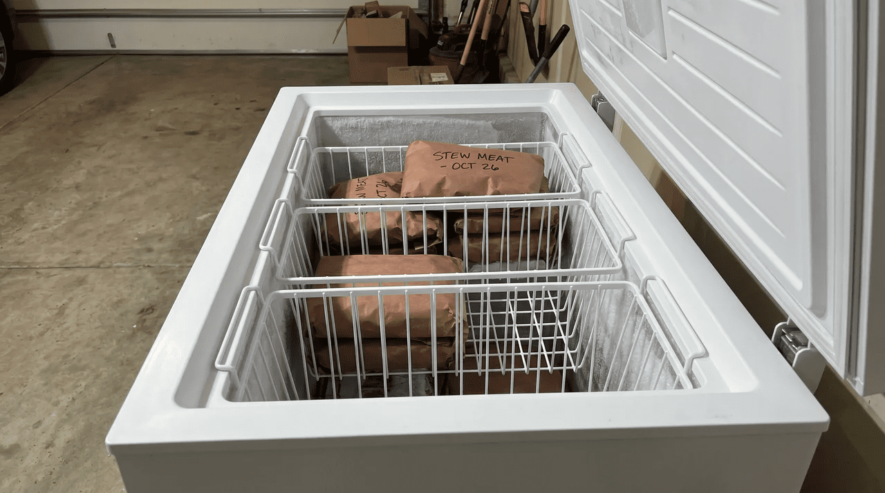 Open chest freezer with three stackable plastic bins partially filled with labeled butcher-paper-wrapped packages