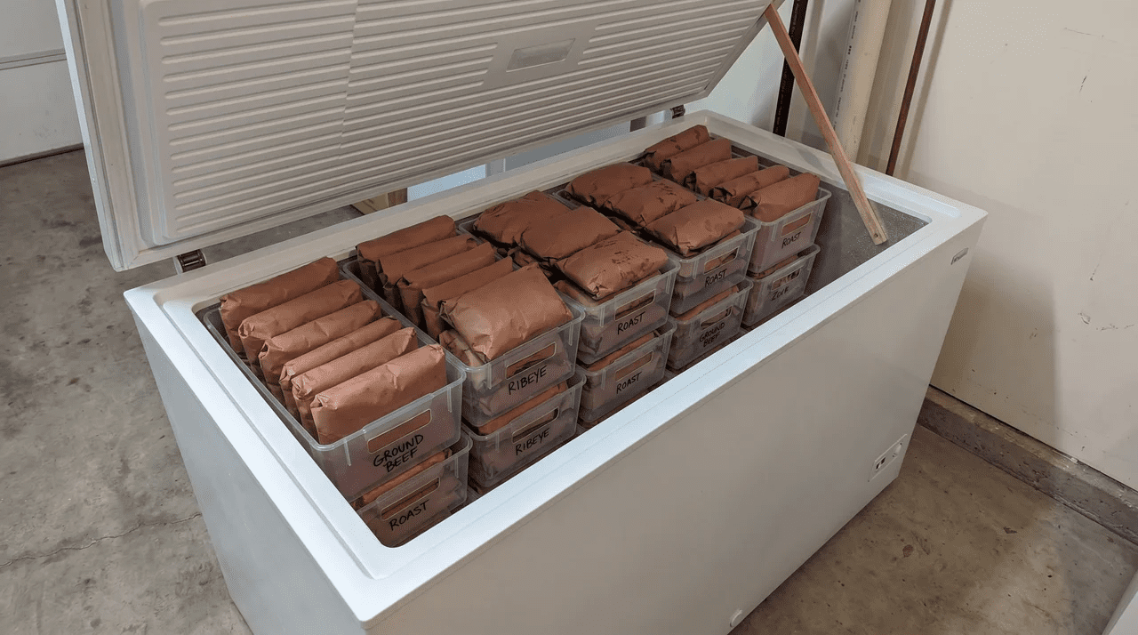 Open chest freezer packed with butcher-paper-wrapped beef packages stacked in plastic freezer bins