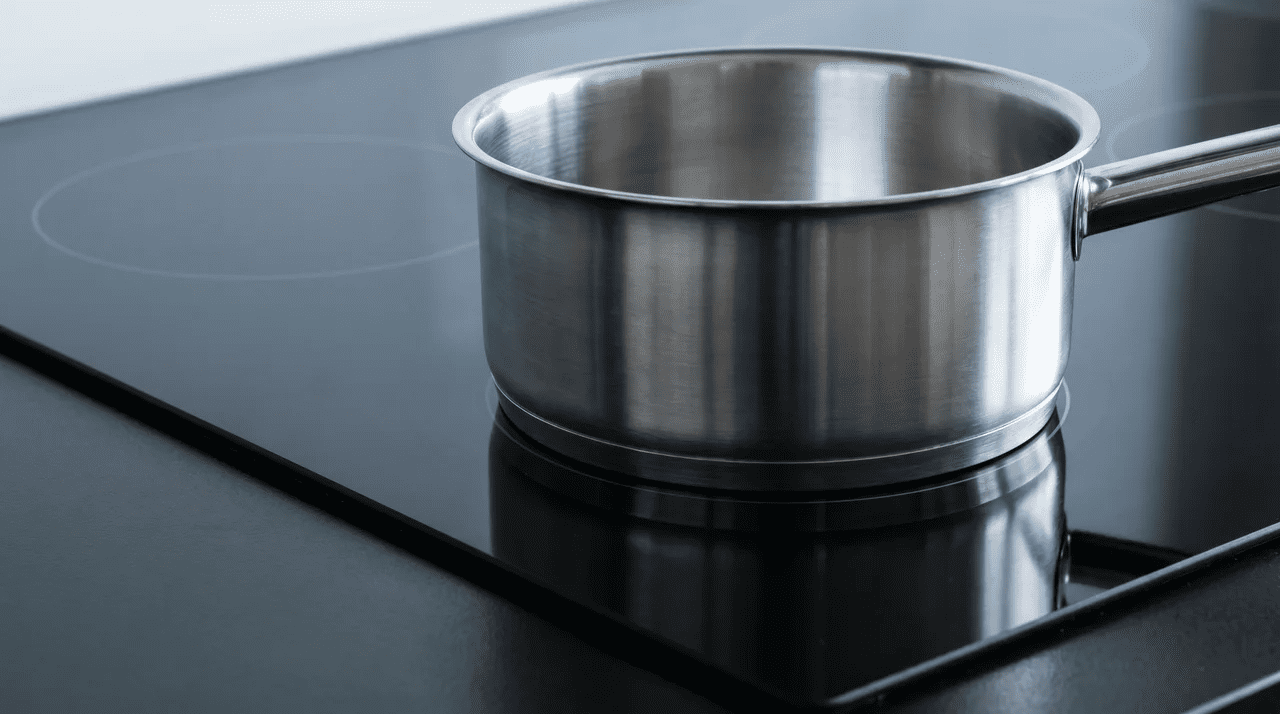 Steel pan resting on a dark glass-ceramic induction zone with no surface glow or visible heat