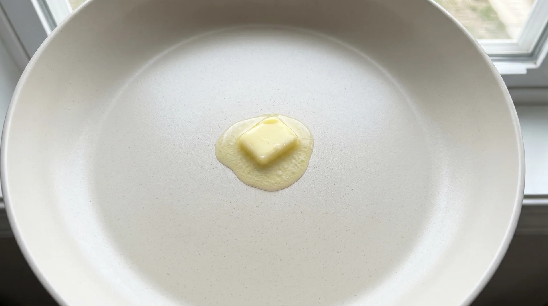 Intact ceramic-coated pan surface with melting butter, good-condition coating visible
