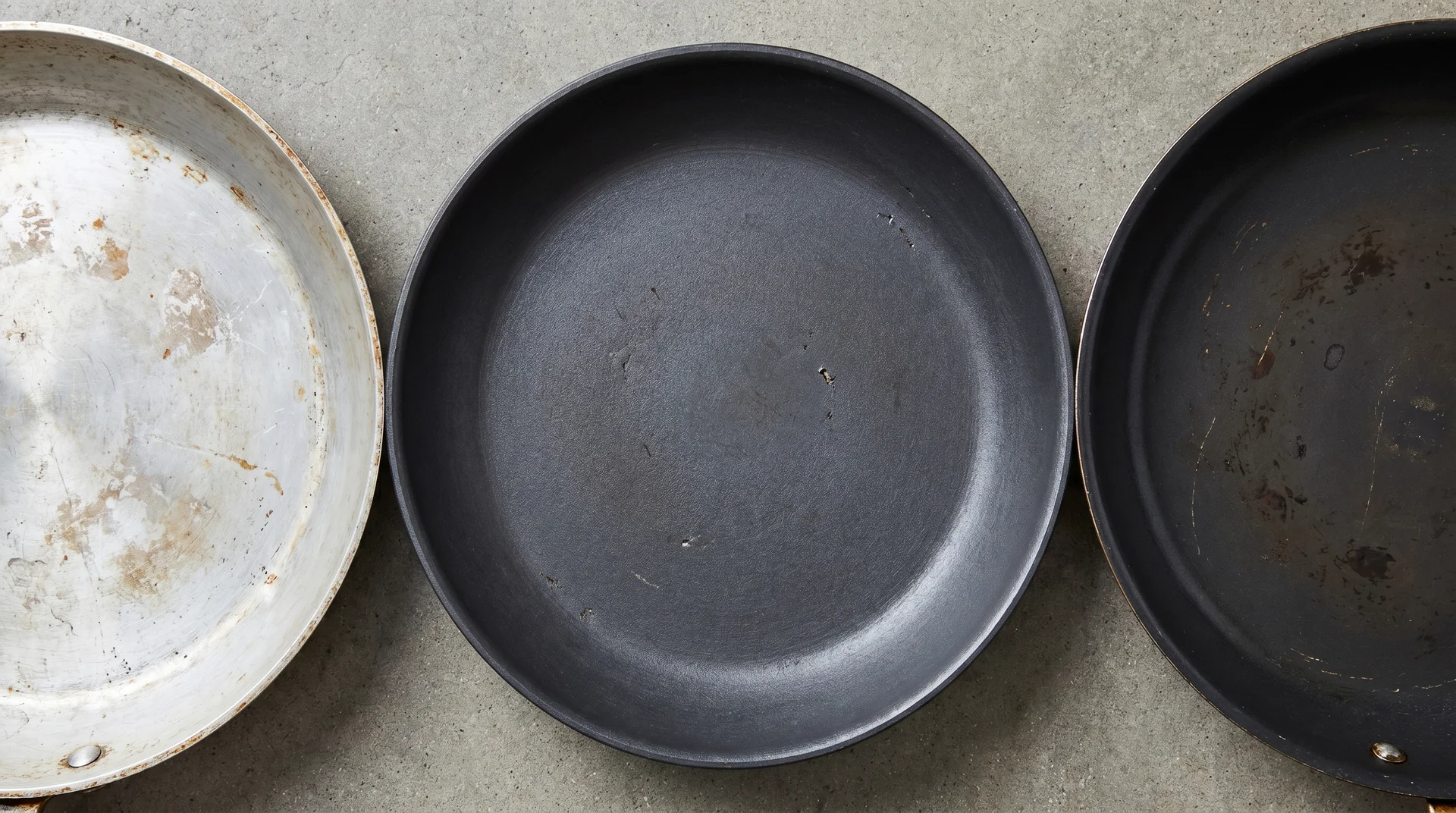 Interiors of bare aluminum, hard anodized, and nonstick pans side by side showing surface texture differences
