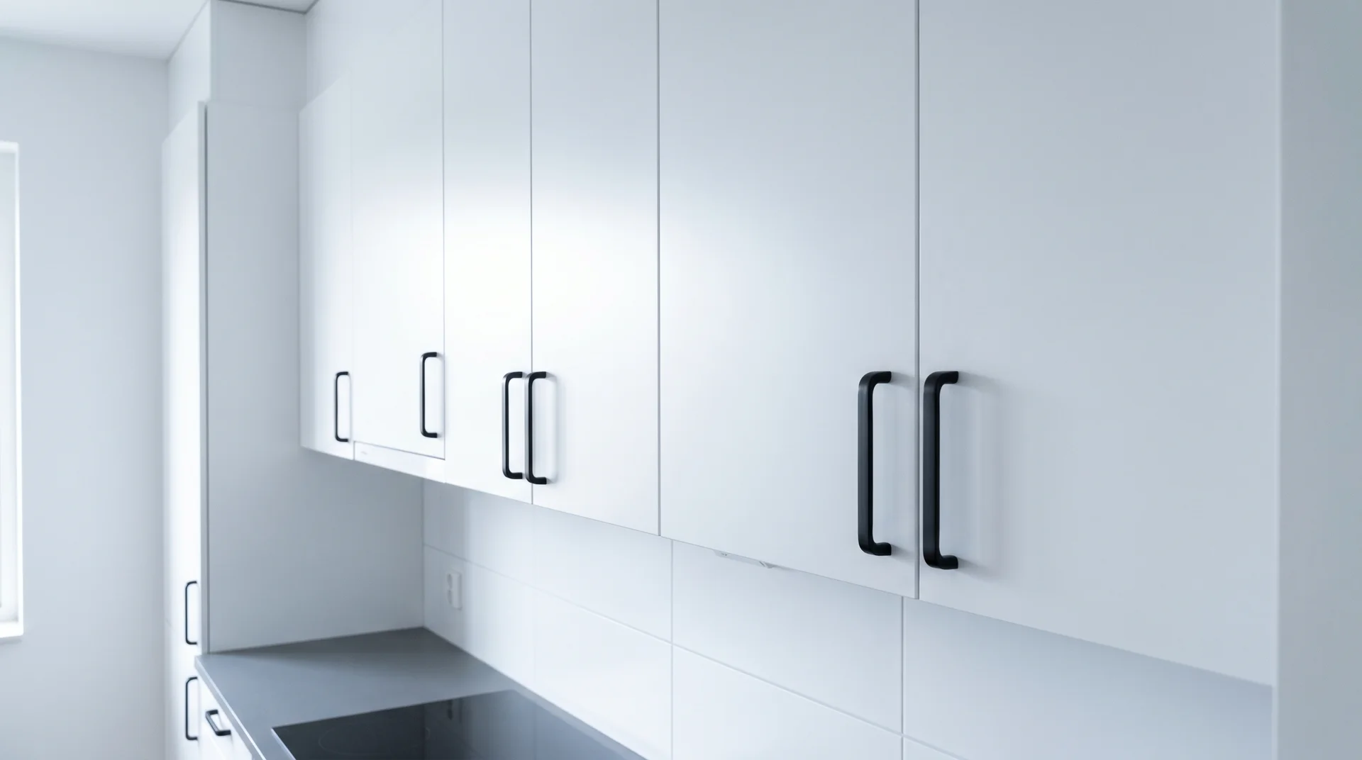Matte black bin pulls on cool bright white upper cabinet doors in a clean modern kitchen with natural daylight 