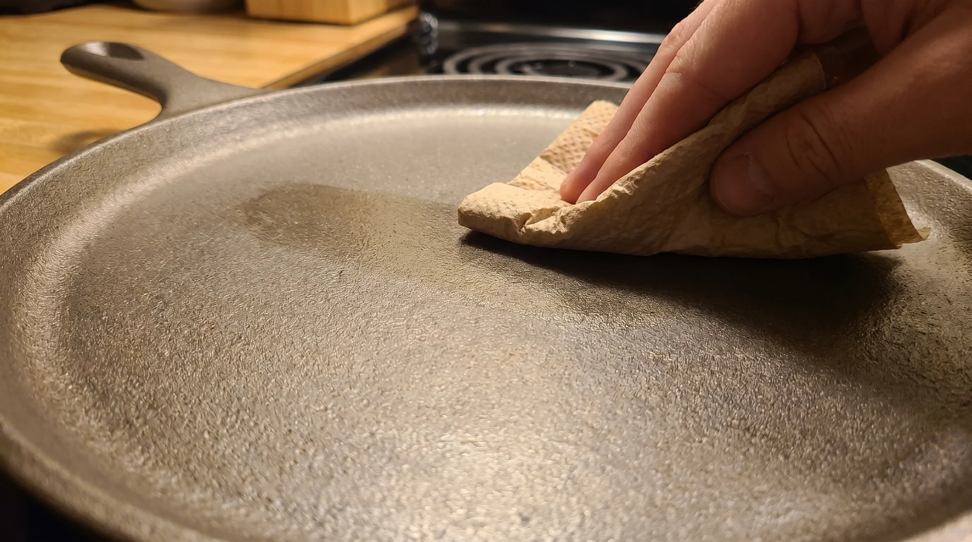 Paper towel buffing a thin oil coat onto a bare cast iron surface during the seasoning process 