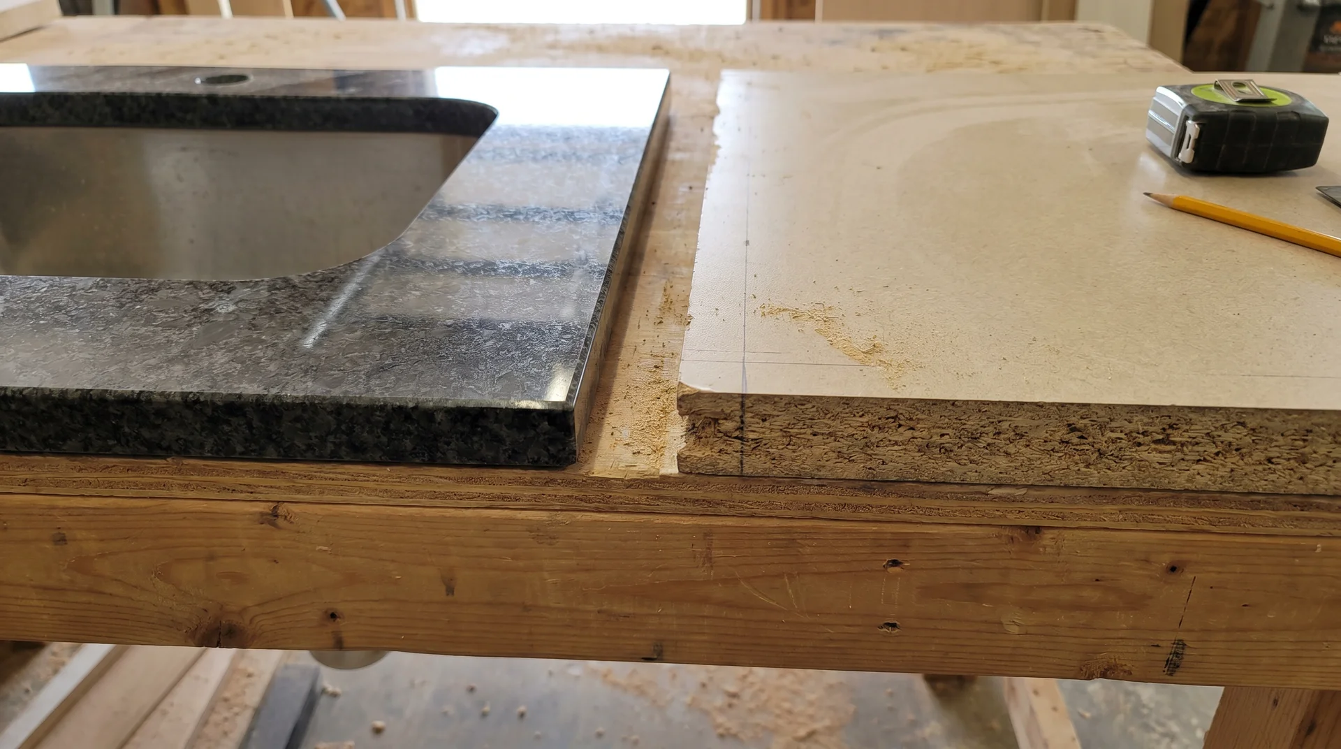 Polished granite countertop edge beside exposed laminate particleboard edge, showing undermount compatibility difference
