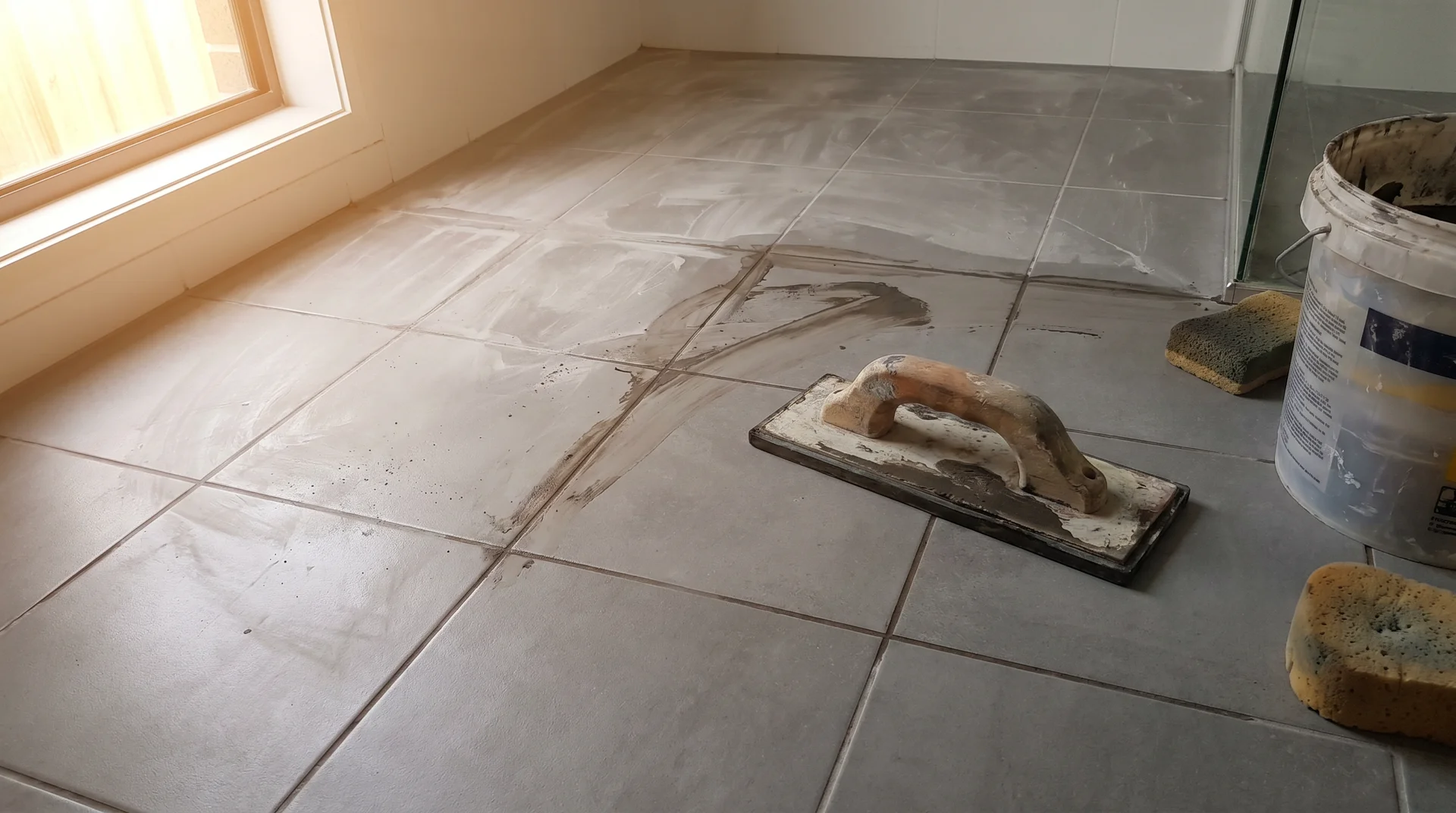Rubber grout float resting on partially grouted bathroom floor tiles mid-project