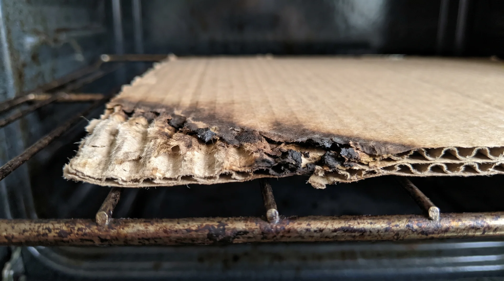 Scorched cardboard edge on an oven rack showing heat damage before ignition point 