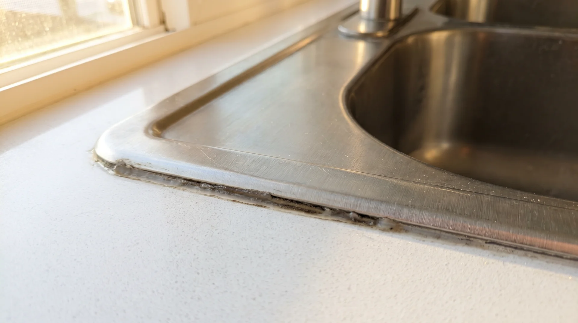 Stainless steel sink showing dark caulk seam between sink rim and countertop where mold commonly grows