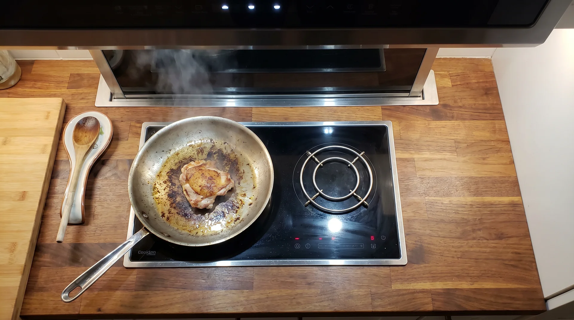 Two-burner induction cooktop in tiny house kitchen with active skillet, range hood above, and narrow prep clearance visible
