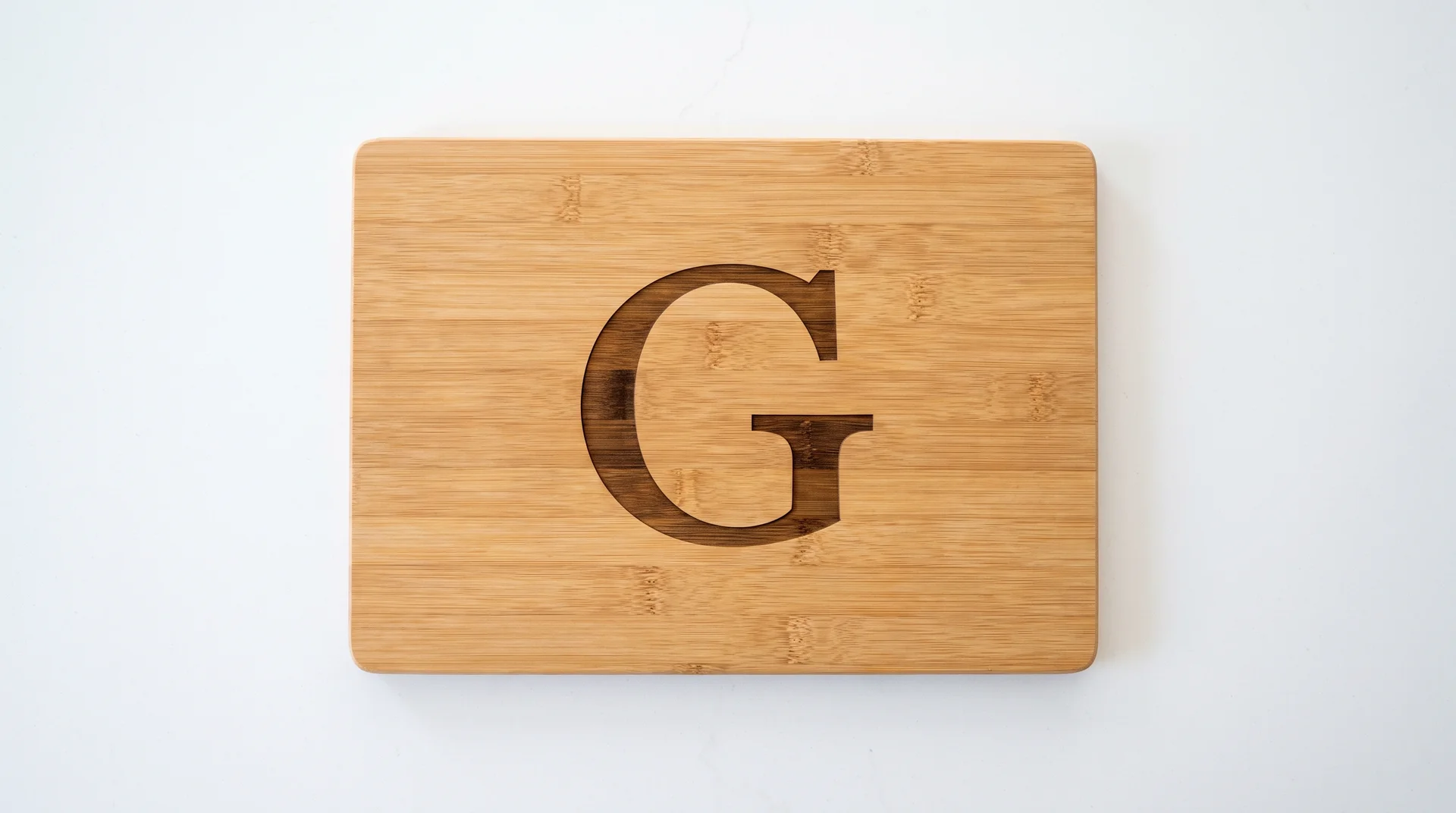 Bamboo board with a single large bold serif initial centered, full board visible, white kitchen counter