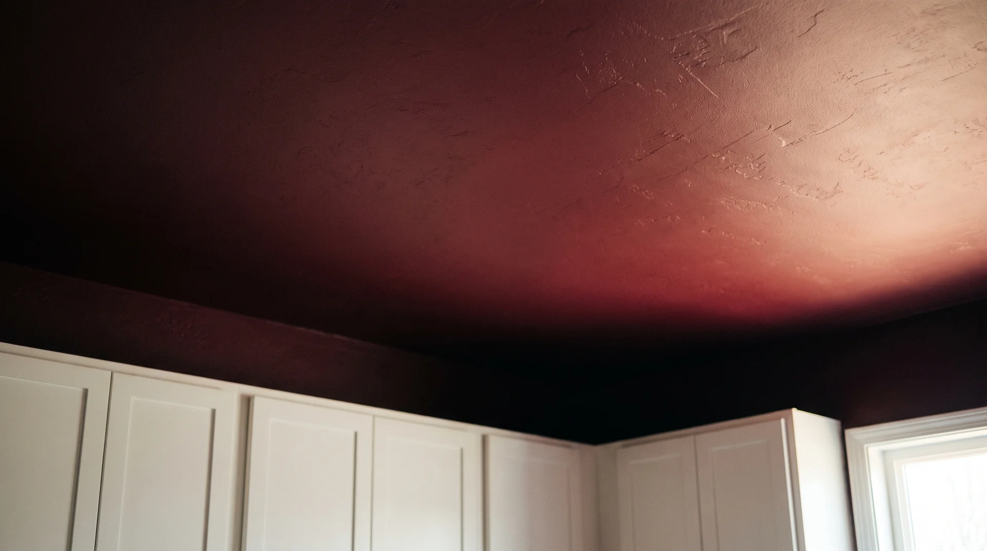 Burgundy ceiling above white Shaker kitchen cabinets with natural light from the right