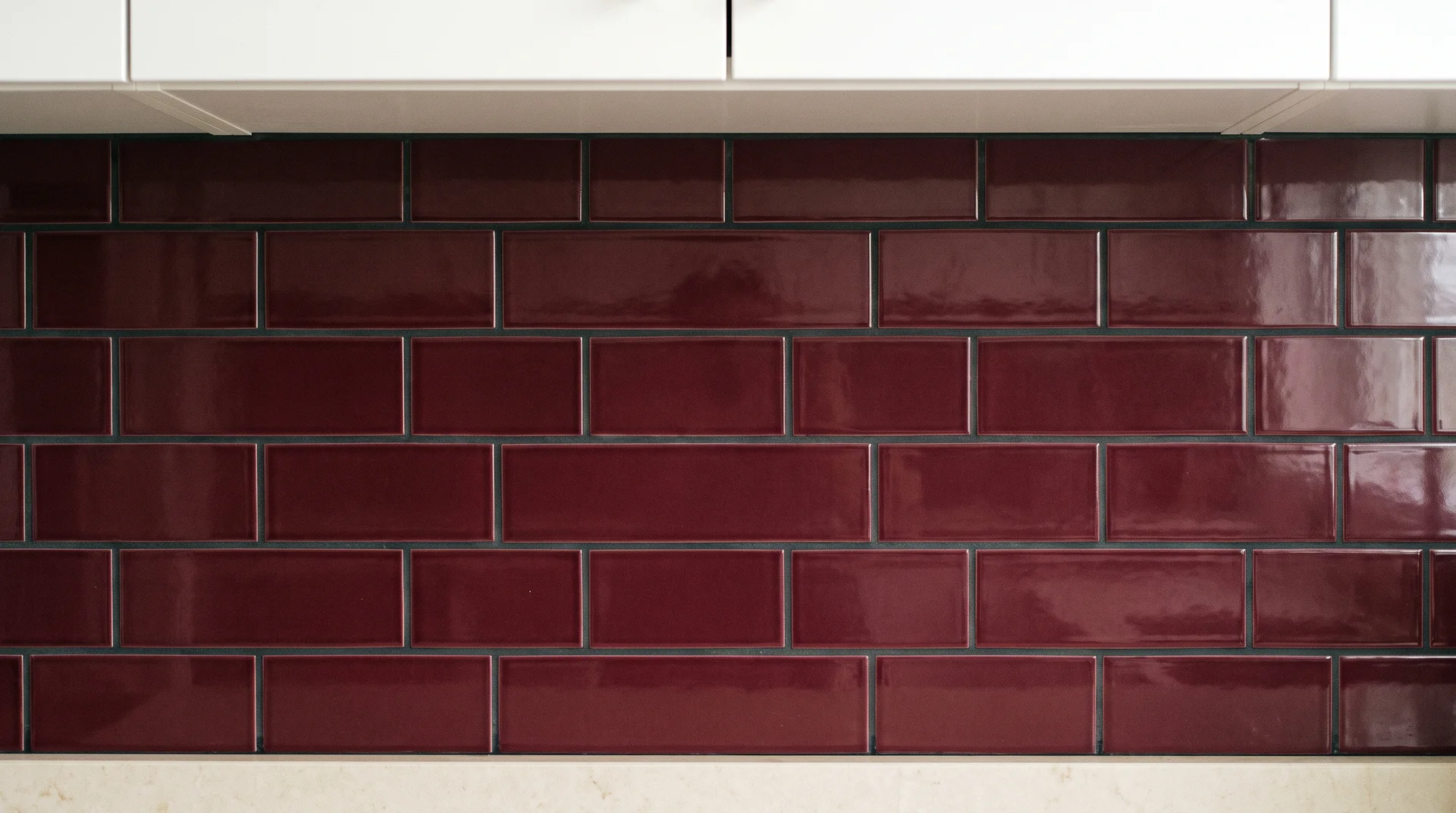 Burgundy ceramic subway tile backsplash in running bond with dark grout ande white cabinet bottom above