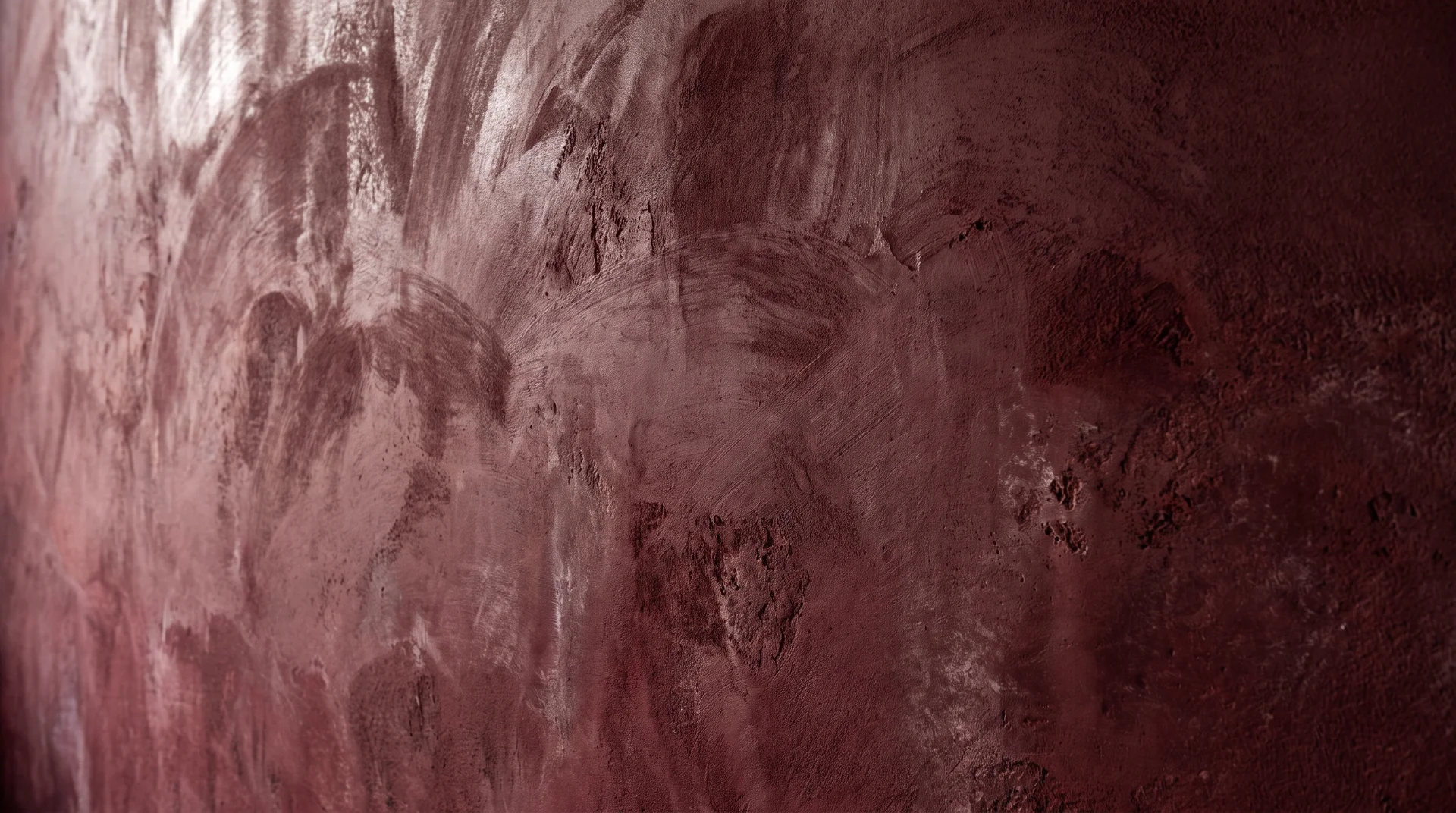 Burgundy limewash wall surface showing texture variation and raking light at close range