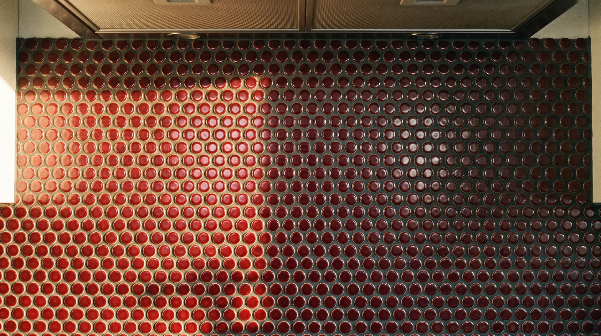 Burgundy penny tile range alcove backsplash in close-up showing dark grout and light variation across tile faces