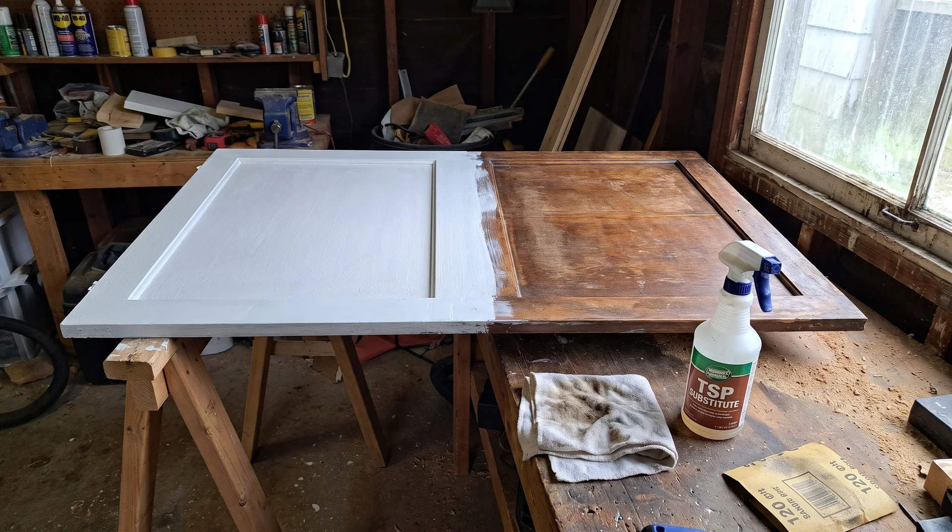 Cabinet door on sawhorses showing bonding primer on one half and original finish on the other during preparation