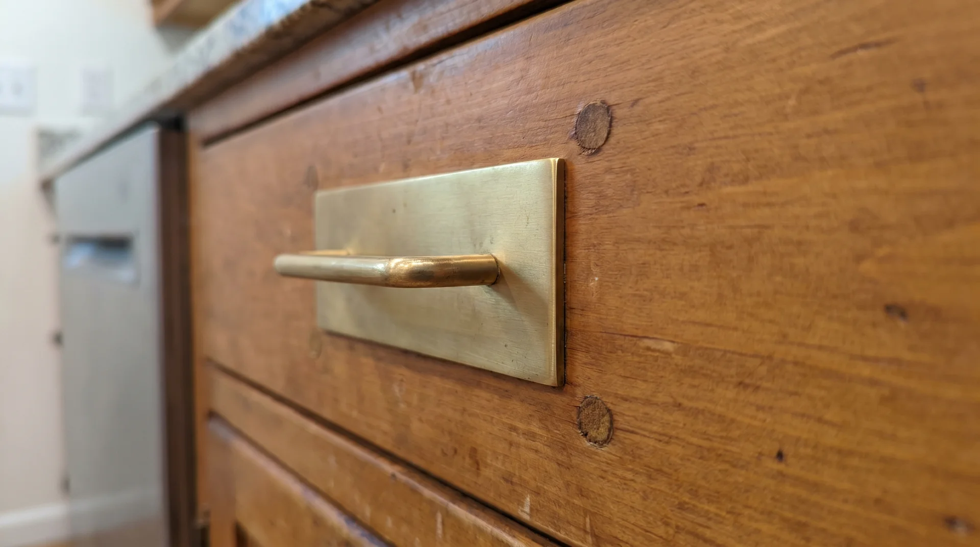 Cabinet pull installed with a backplate covering previous hardware holes on a drawer face.