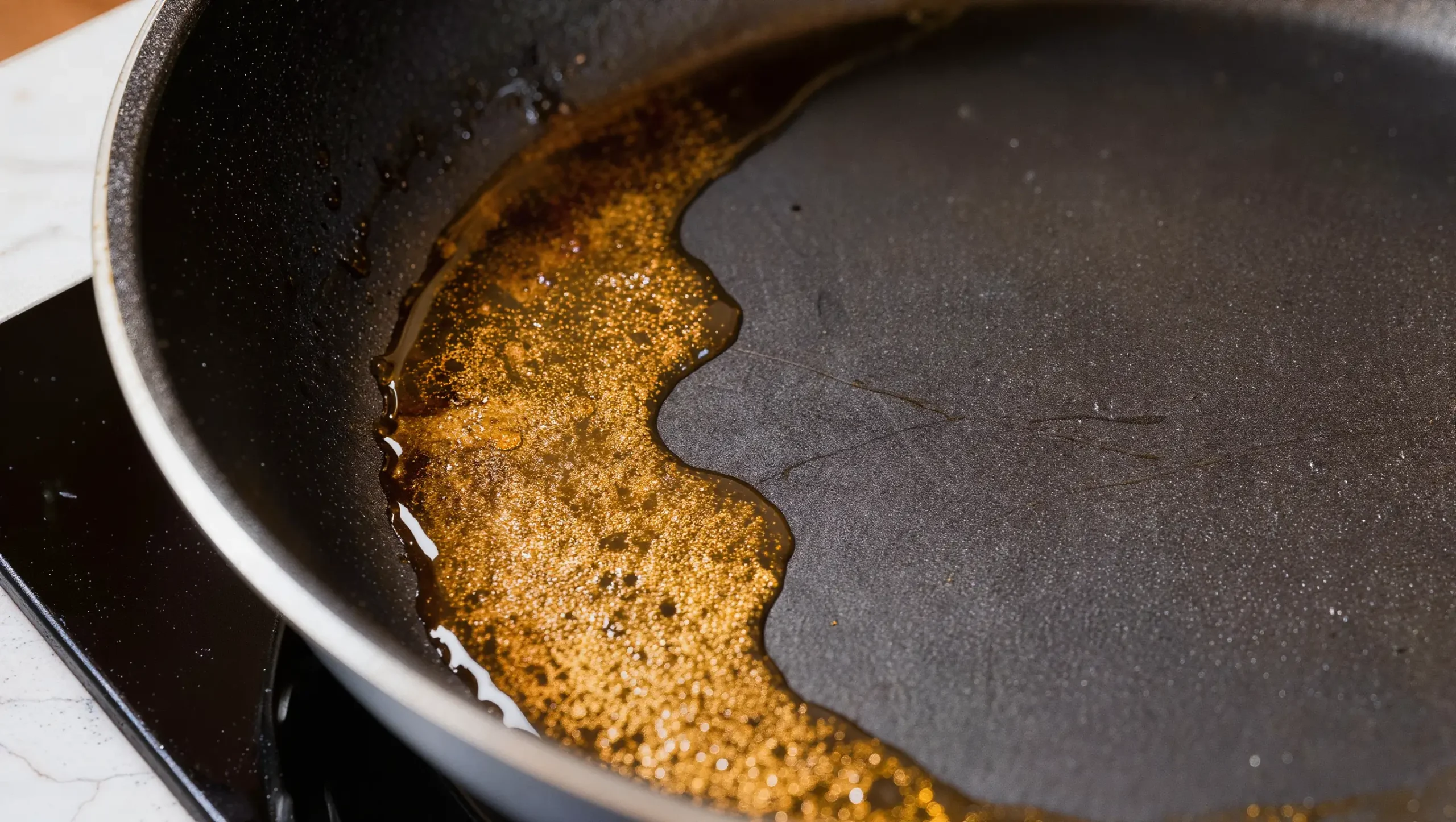 Close-up of hard anodized pan interior showing aerosol spray residue buildup — golden-brown film contrasted with clean surface area