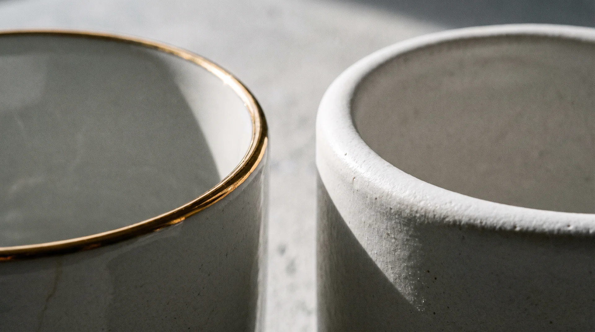 Close-up of two ceramic mug rims side by side, one with a gold metallic rim, one plain white, showing the difference