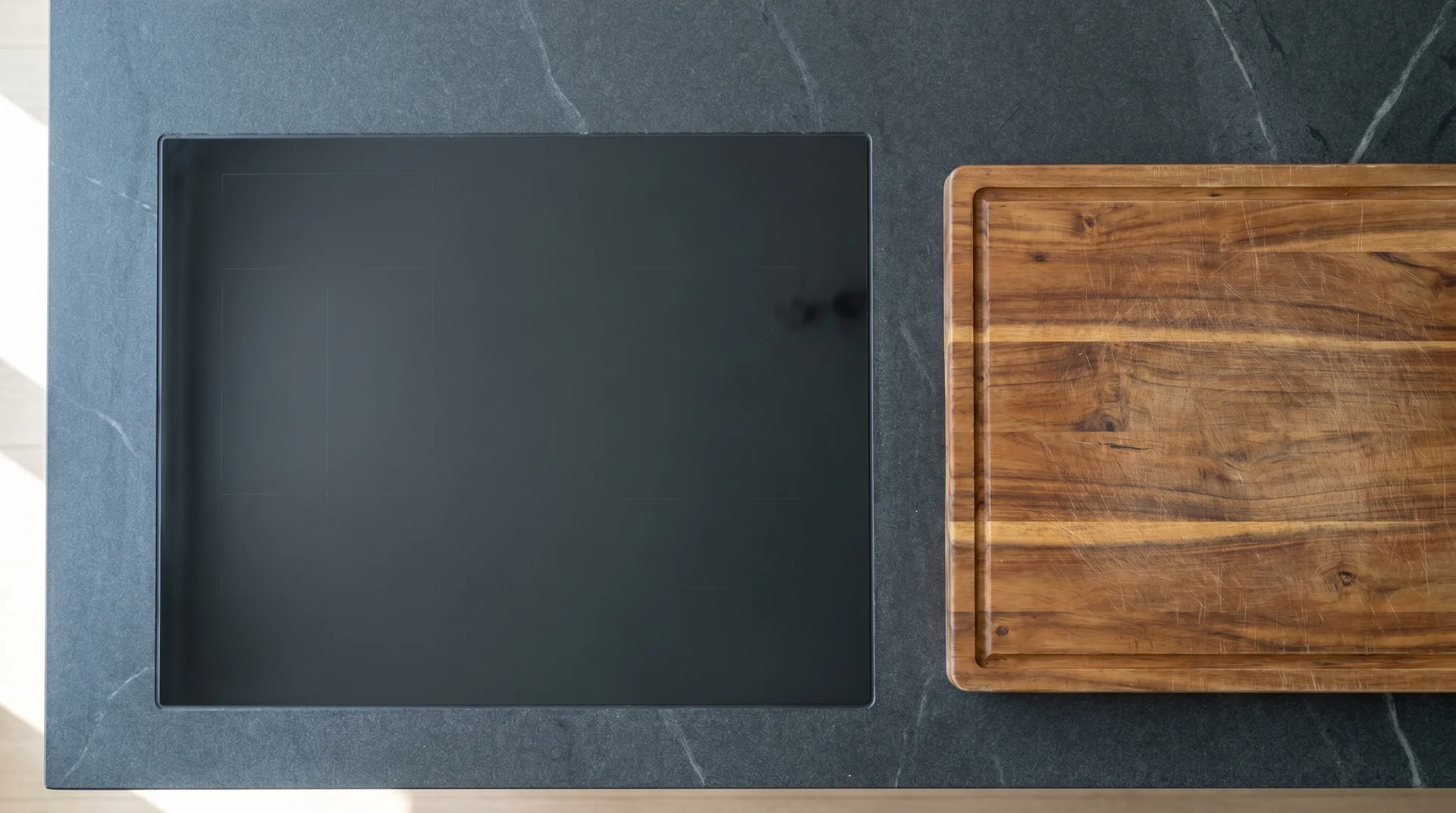 Cutting board resting directly on flush induction cooktop surface in kitchen island, showing dual-use counter space