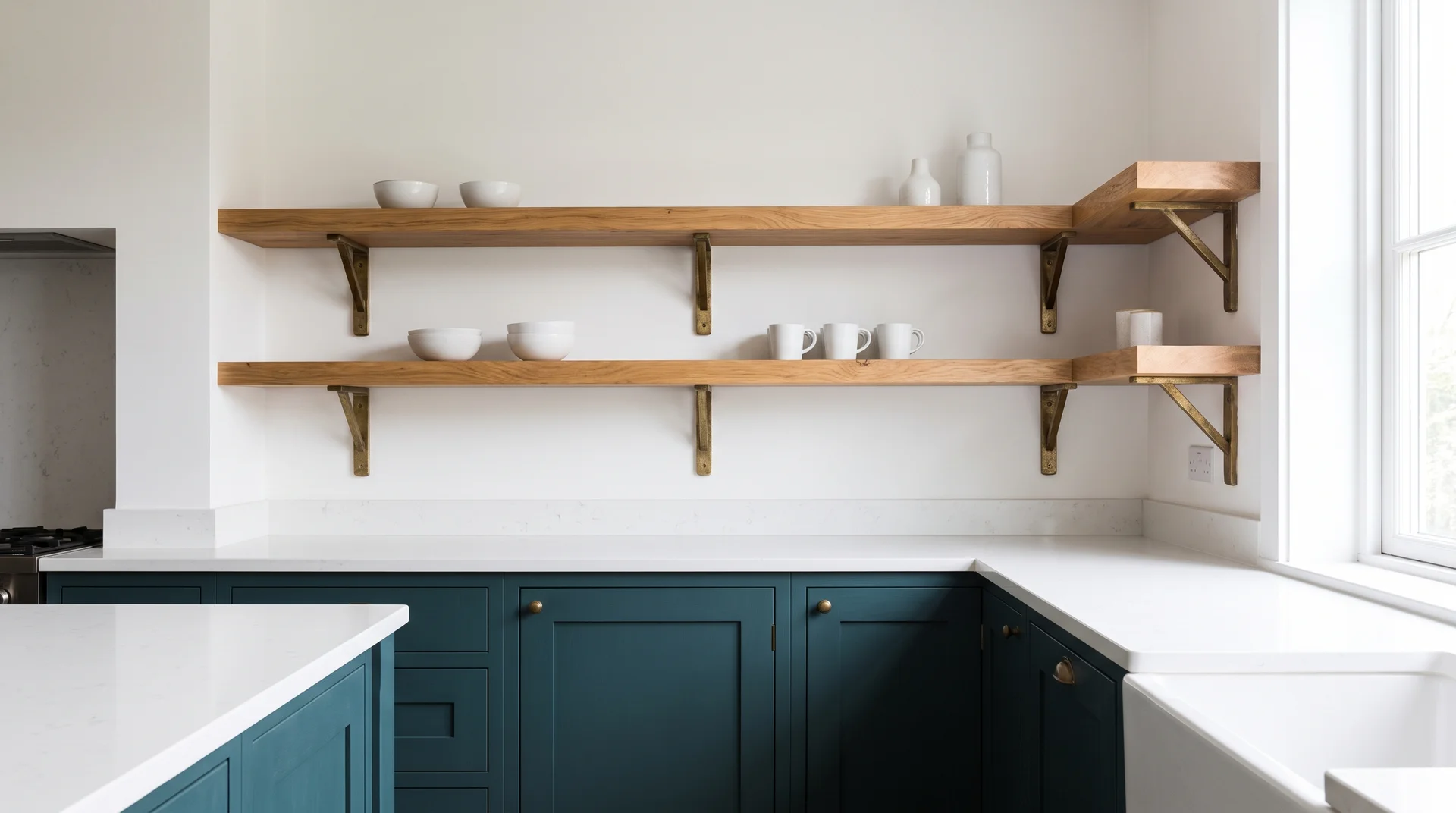 Dark teal lower cabinets with natural oak floating shelves above on a white wall with brass shelf brackets