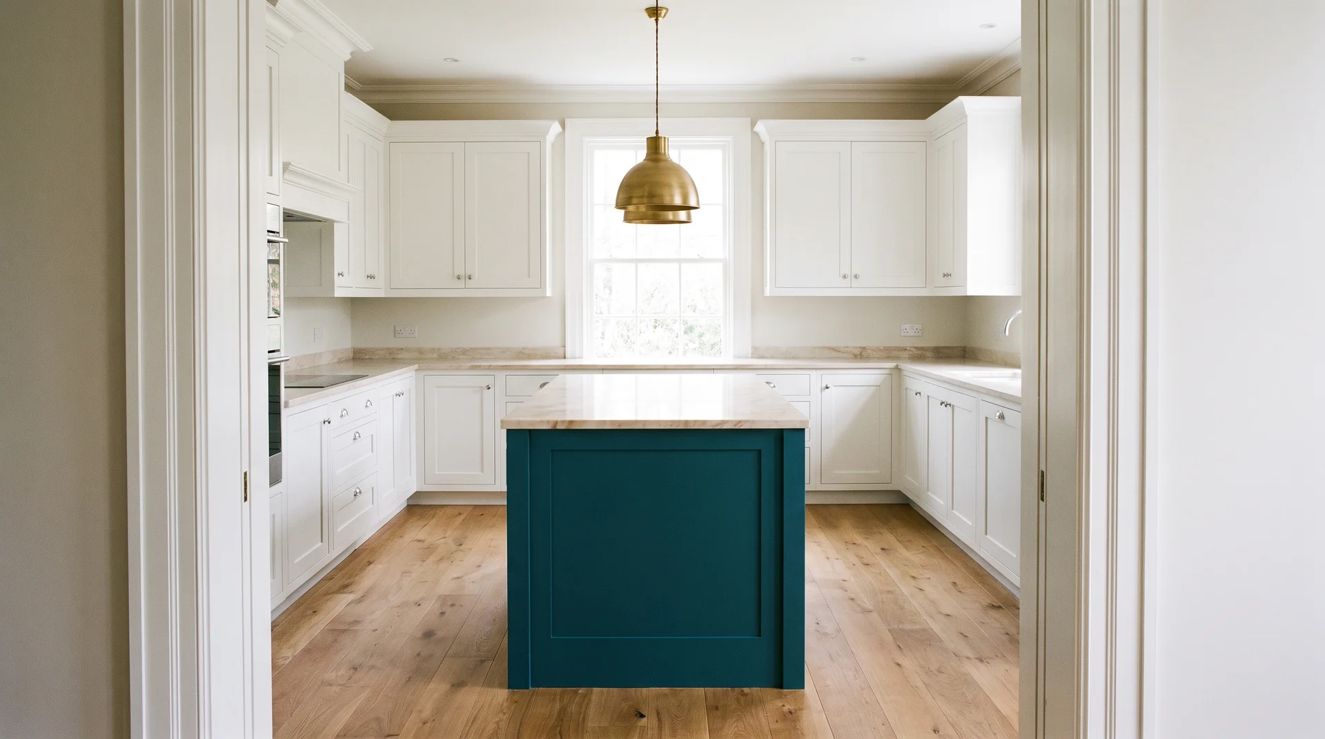 Deep teal kitchen island with marble countertop against all-white perimeter cabinets and brass pendant light