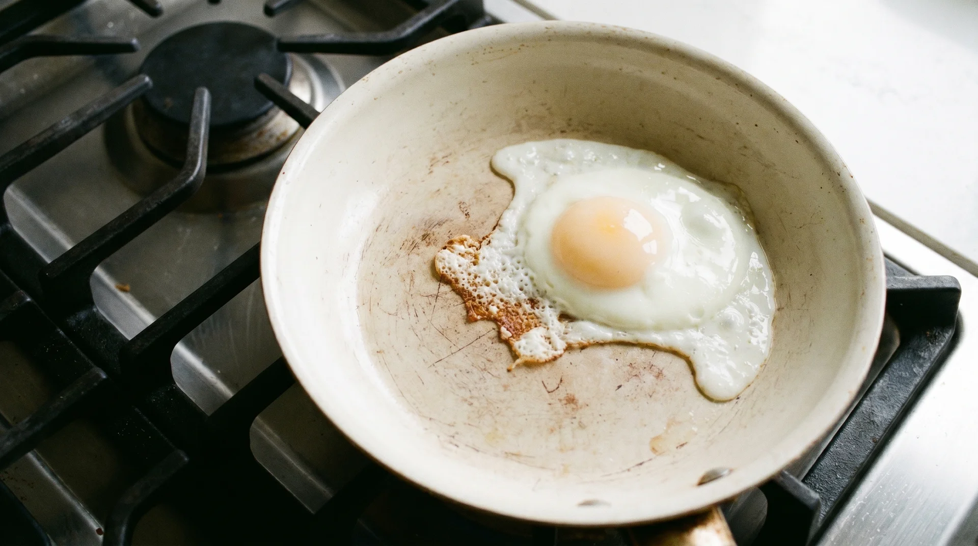 Egg sticking in worn spot of ceramic pan showing localized nonstick coating loss