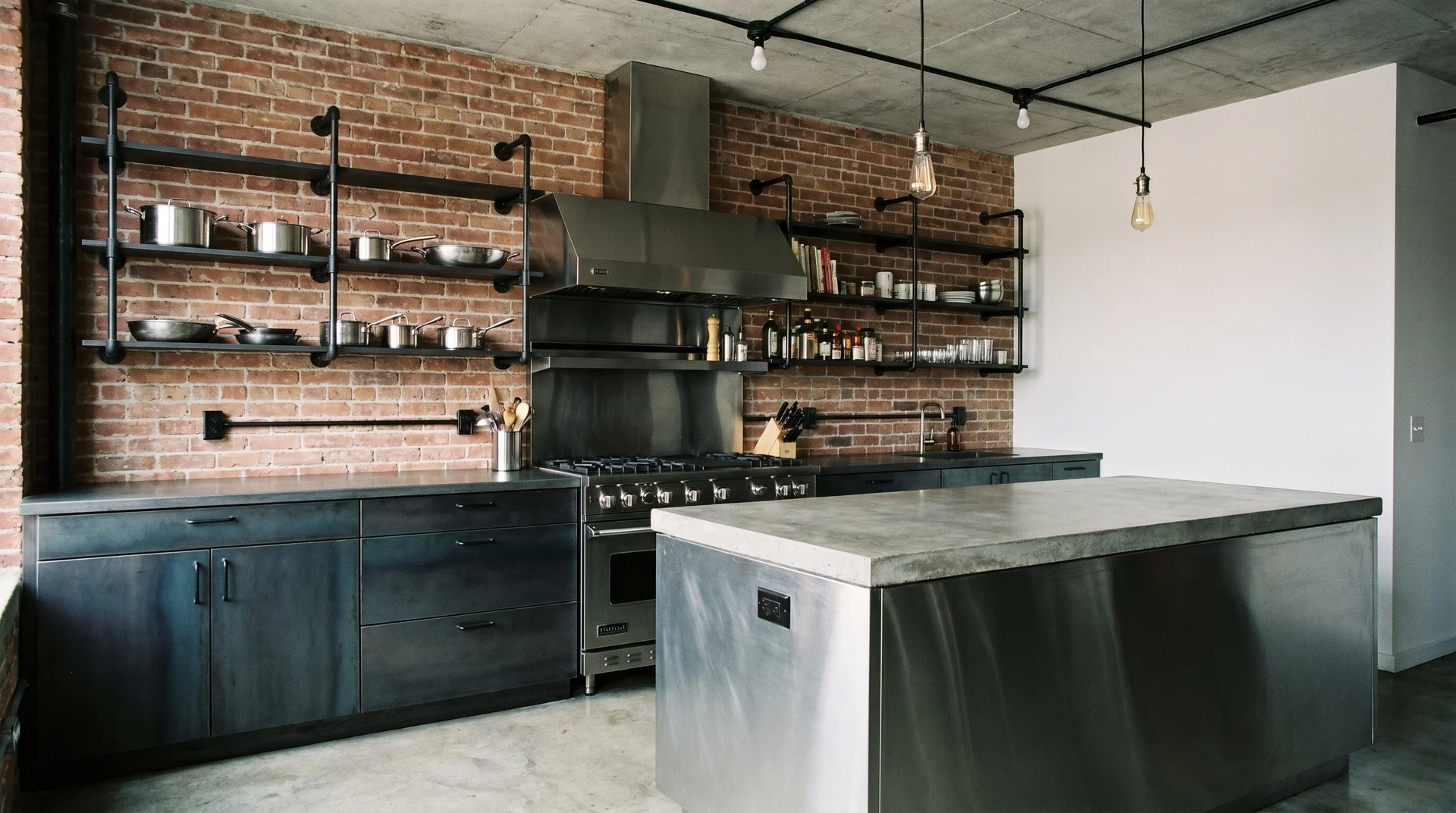 Exposed brick wall with matte black pipe shelving and exposed-bulb pendants in an industrial kitchen