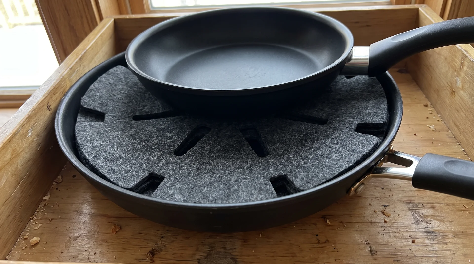 Felt pan protector between two stacked nonstick pans in a kitchen cabinet, showing correct storage to prevent scratching