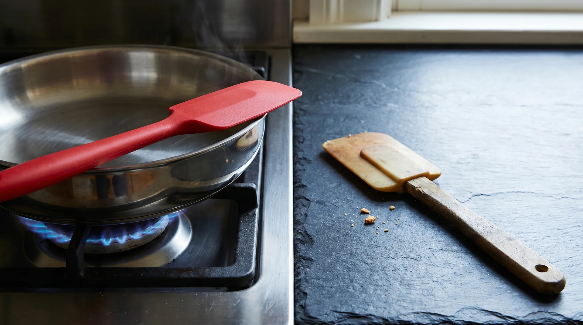 Food-grade silicone scraper near a hot pan next to a natural rubber scraper kept away from heat