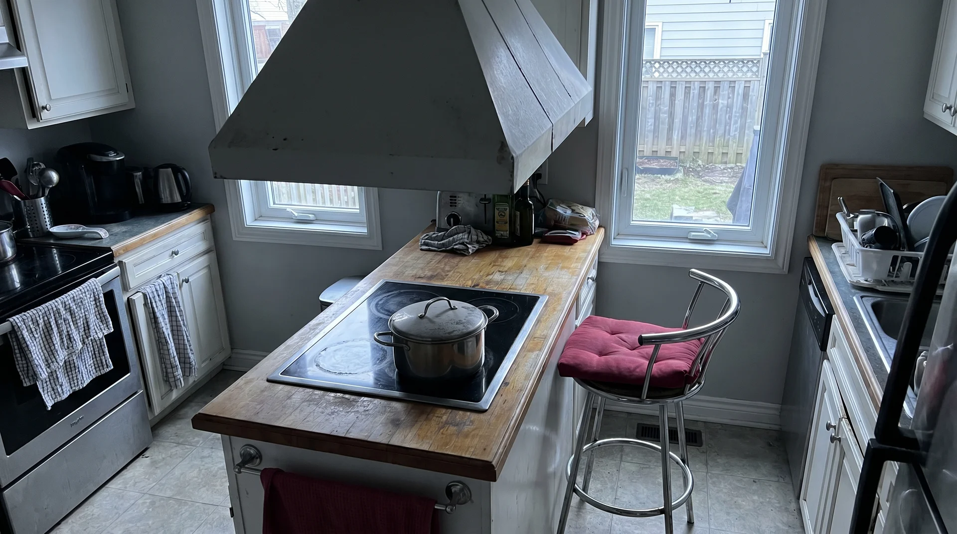 Kitchen island with cooktop showing insufficient clearance and visual clutter from competing range hood