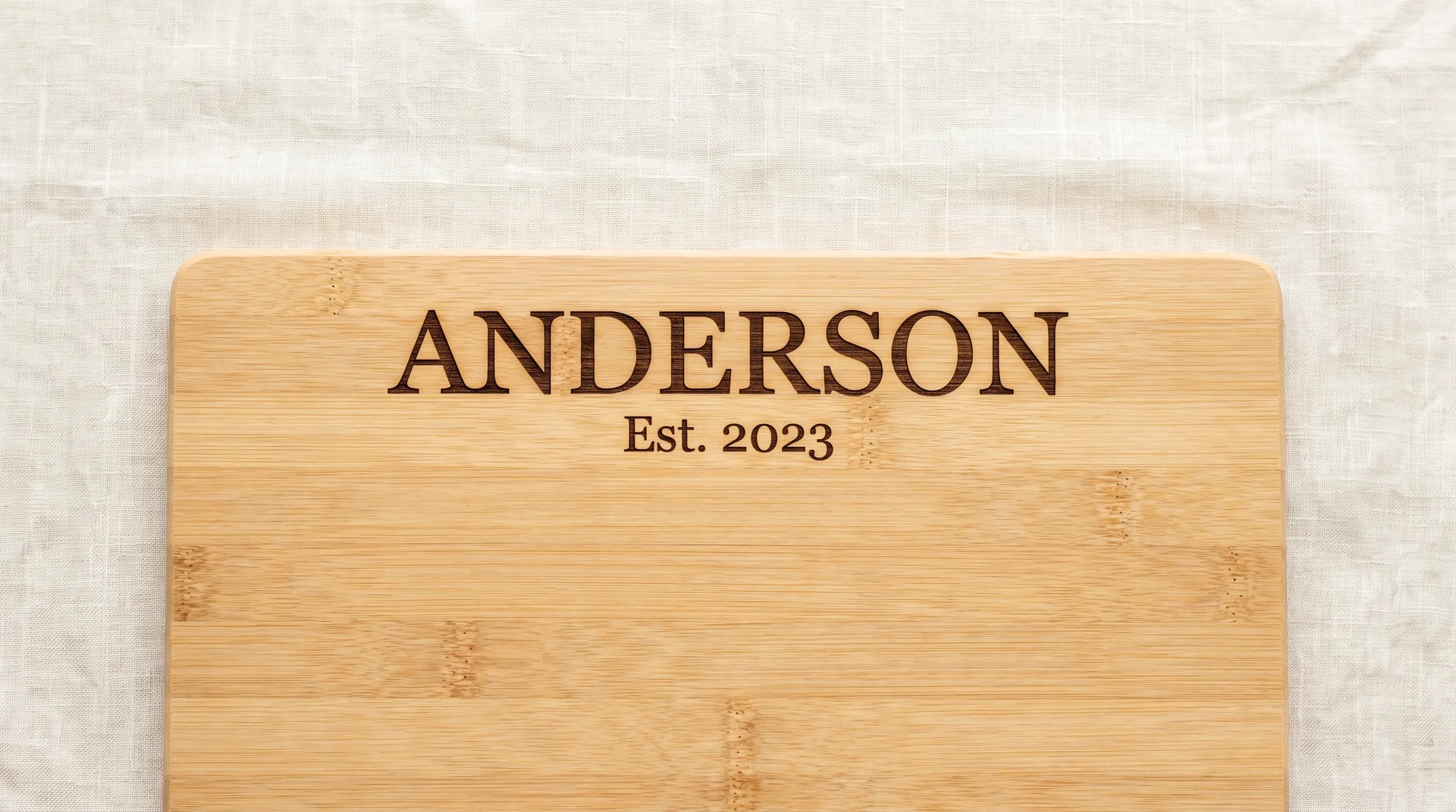 Light bamboo board with family surname larger above and Est. year smaller below, cream linen surface