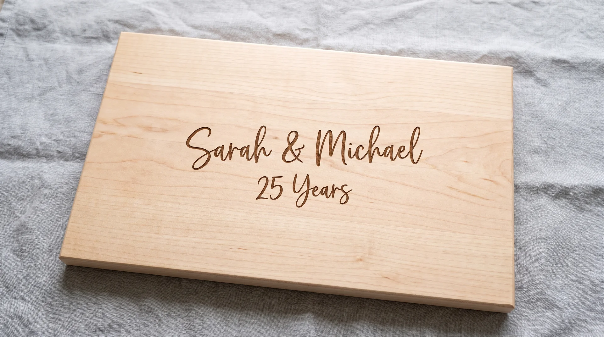 Light maple board with two names and an ampersand above and '25 Years' below, gray linen, overhead light