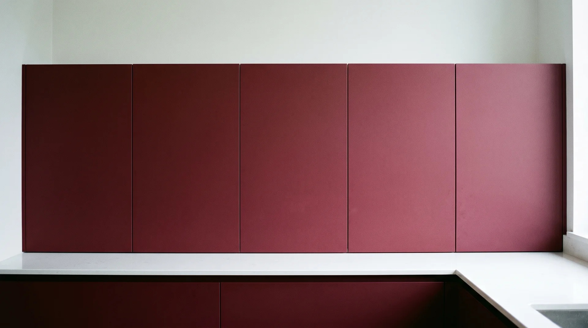 Modern flat-front burgundy kitchen cabinets with no visible hardware in diffused natural light