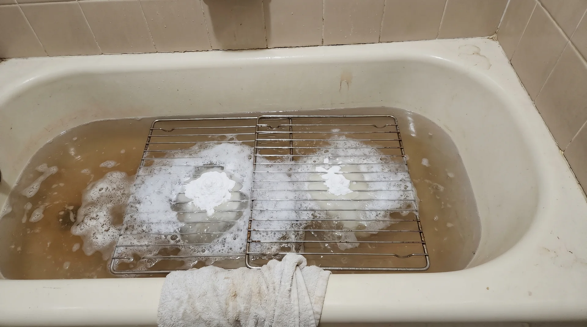 Oven racks soaking in a bathtub with baking soda and vinegar solution