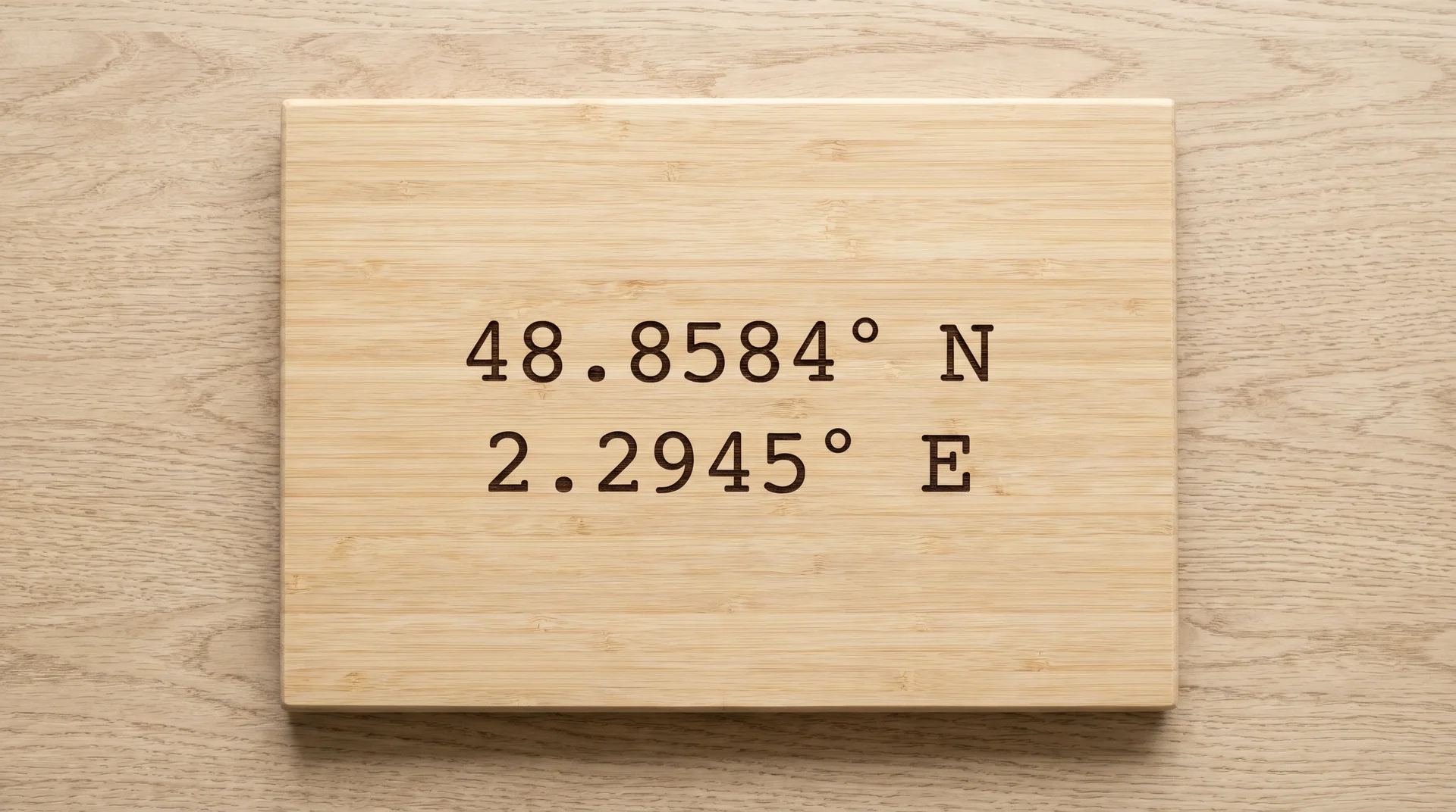 Pale bamboo board with two lines of decimal GPS coordinates in clean monospace type, centered