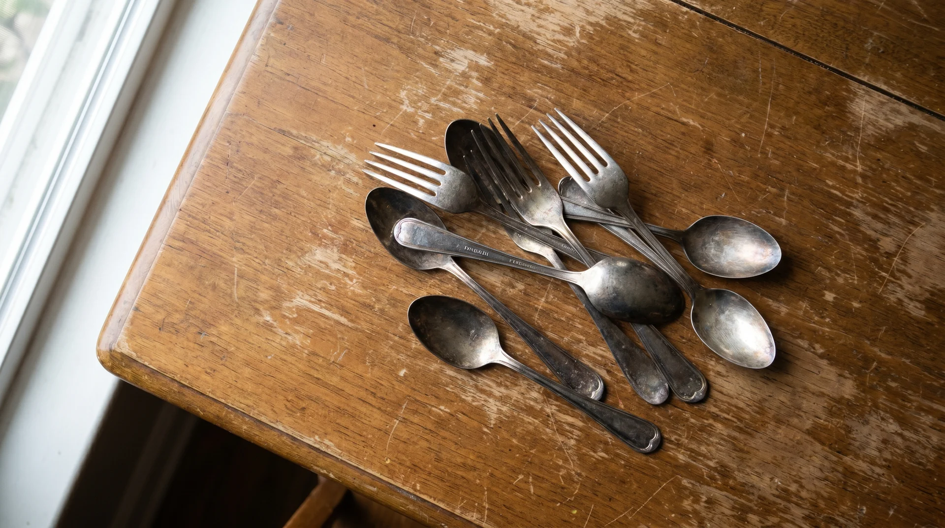Silver plated flatware scattered on a wood table showing tarnish and handle stamps