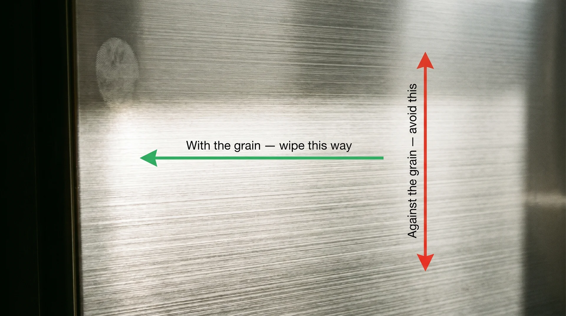 Stainless steel refrigerator surface under raking light showing horizontal grain lines with directional wipe arrows annotated