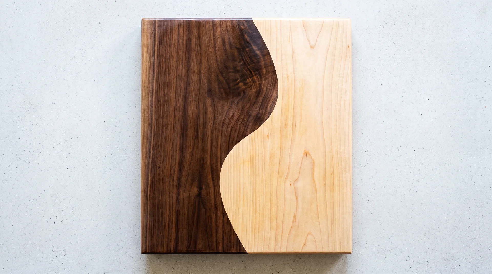 Two-species cutting board with organic S-curve boundary between dark walnut and pale maple halves