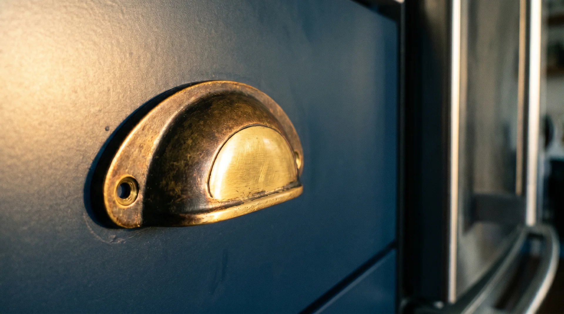 Unlacquered brass cup pull showing natural patina darkened at grip contact points with recessed areas remaining bright