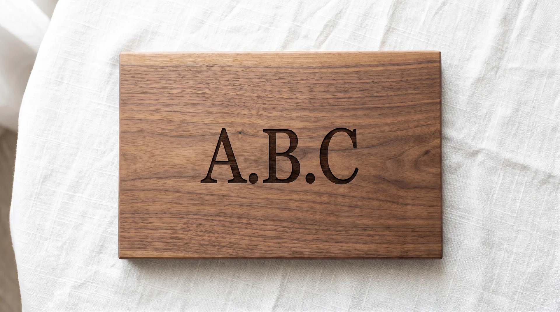 Walnut board with a clean three-letter serif monogram centered, white linen, diffused side window light