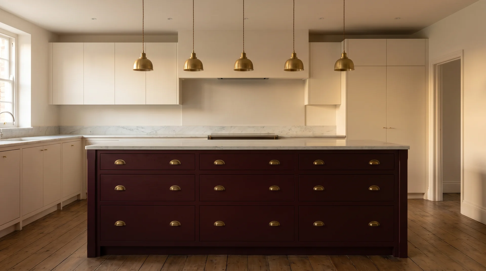 Warm white kitchen with a deep burgundy Heritage Red island, unlacquered brass hardware, calm marble countertop, afternoon light